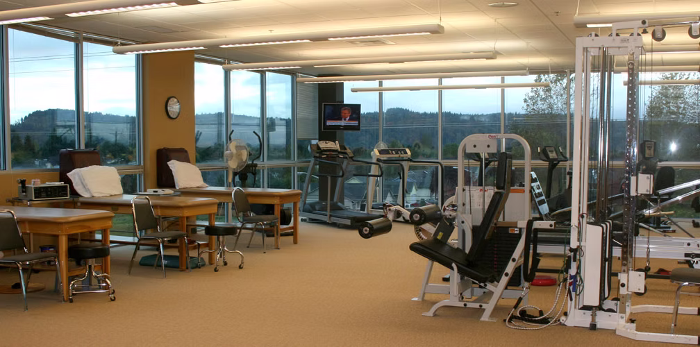 The treatment floor at Peak Orthopedic & Sports Physical Therapy, with treatment tables, treadmills, and strength equipment beside a wall of windows